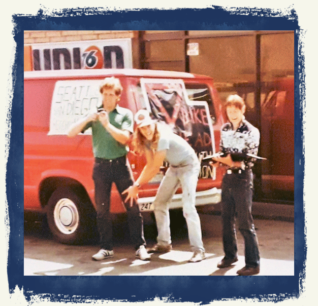Photo showing the three crew members with the van behind them. The van includes two banners: "Seattle to San Diego" on the side and "Bike ahead, pass with caution" on the back.